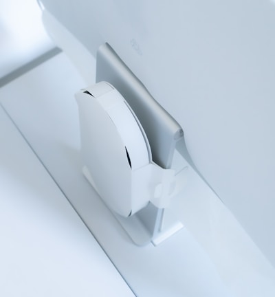 A white, sleek, vertical gaming console placed beside a large, slim monitor. The setting exudes minimalism with a focus on modern technology design.