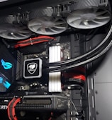 A high-performance gaming computer setup showing the interior components, including a GeForce RTX graphics card, cooling system with three fans, a motherboard, and visible wiring with red and black cables.